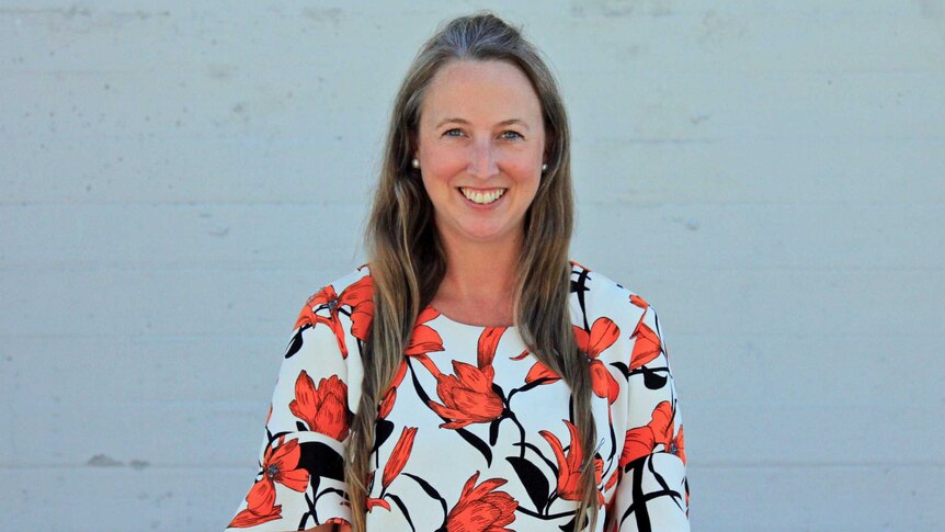 A woman smiling standing in front of a grey wall