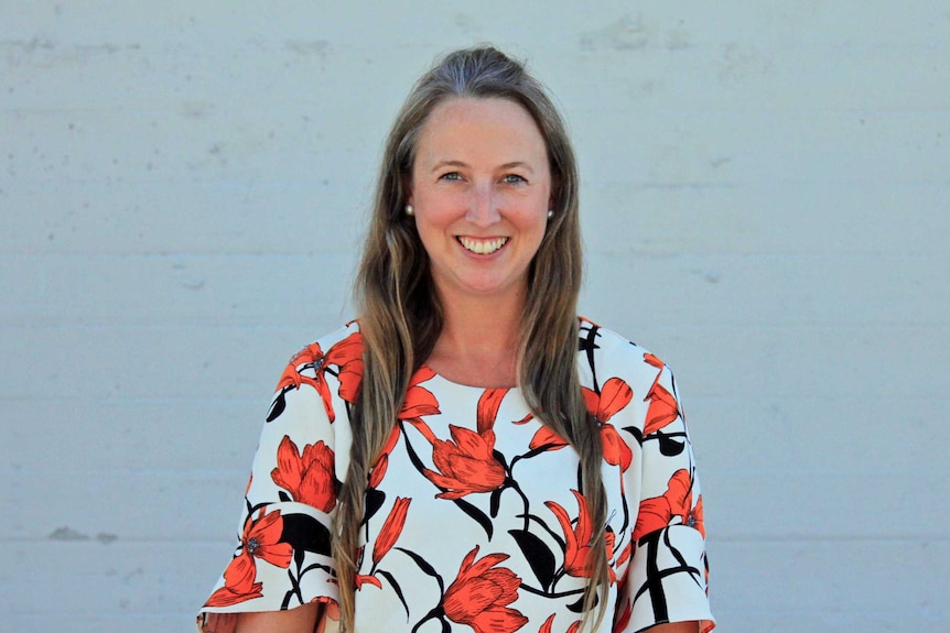 A woman smiling standing in front of a grey wall