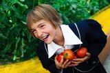 A young child smiles in a garden holding homegrown tomatoes she has harvested, easy veggies to grow with kids.