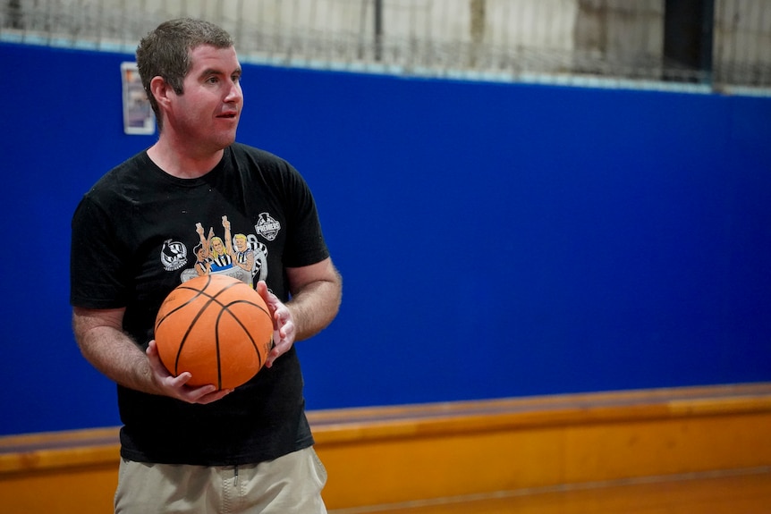 A man wearing a black t-shirt holds a basketball on the court.