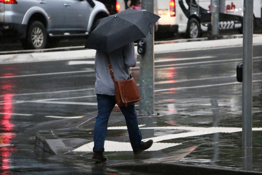 A man walks along a South Brisbane street in the rain.