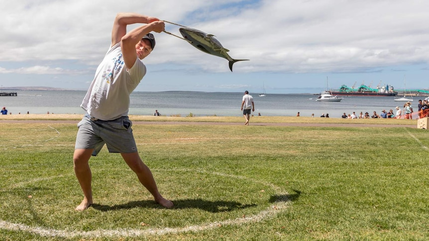 A man tossing a false, heavy tuna across a soft patch of grass.