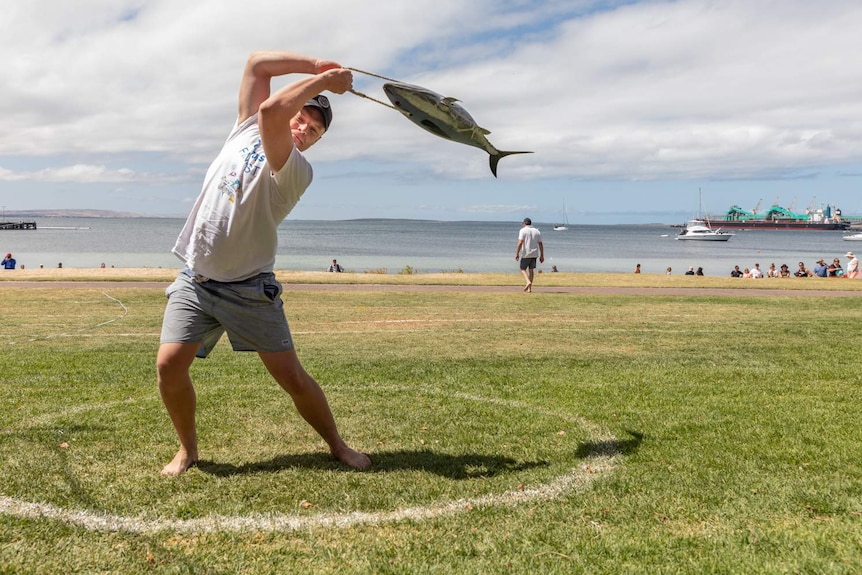 A man tossing a false, heavy tuna across a soft patch of grass