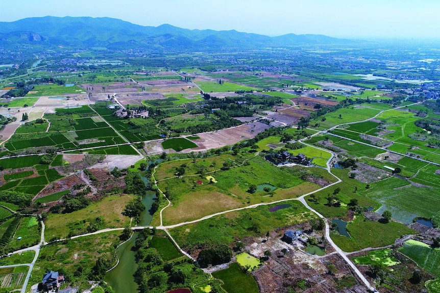 An aerial view of green areas divided by loads and surrounded by mountains.