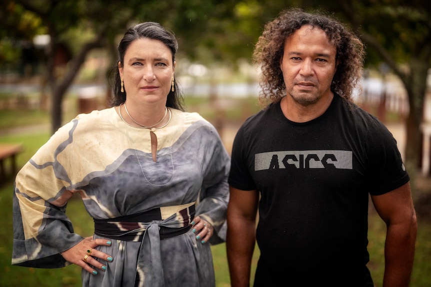 Woman in a white and blue dress with her hands on her hips standing next to a man in a black t-shirt.