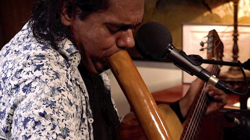 A man plays the didgeridu and guitar.