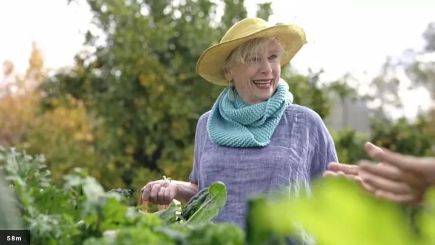 A woman wearing a hat, standing in a garden.