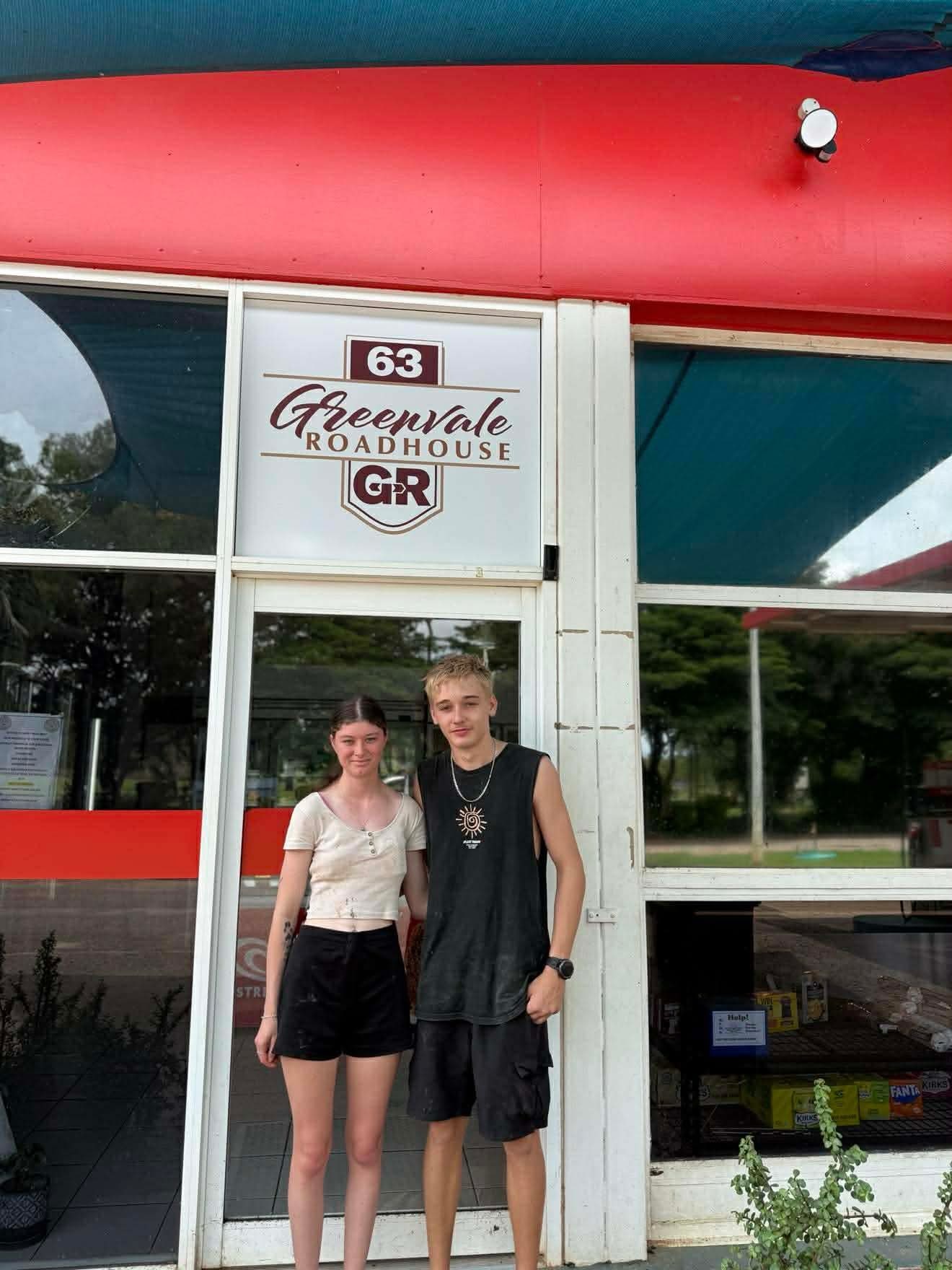 Um jovem casal está em frente a um bar à beira da estrada.