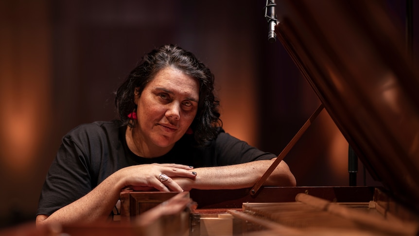Yuwaalaraay composer Nardi Simpson sits at a grand piano with her arms resting crossed on the music stand. 