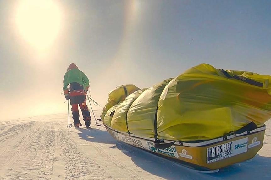 Colin O'Brady pulls a yellow sled as he walks towards the sunlight.