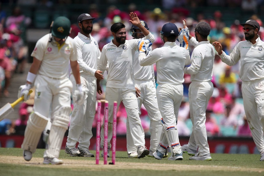 Australia batsman Marcus Harris walks past his broken stumps during the SCG Test as India players celebrate in the background.