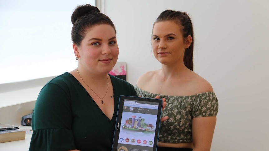 Two women stand next to each other holding an iPad with a new online portal for out-of-home care on the screen