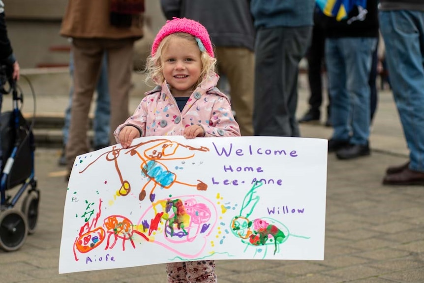 A young girl holds a home made sign which says welcome home lee-anne