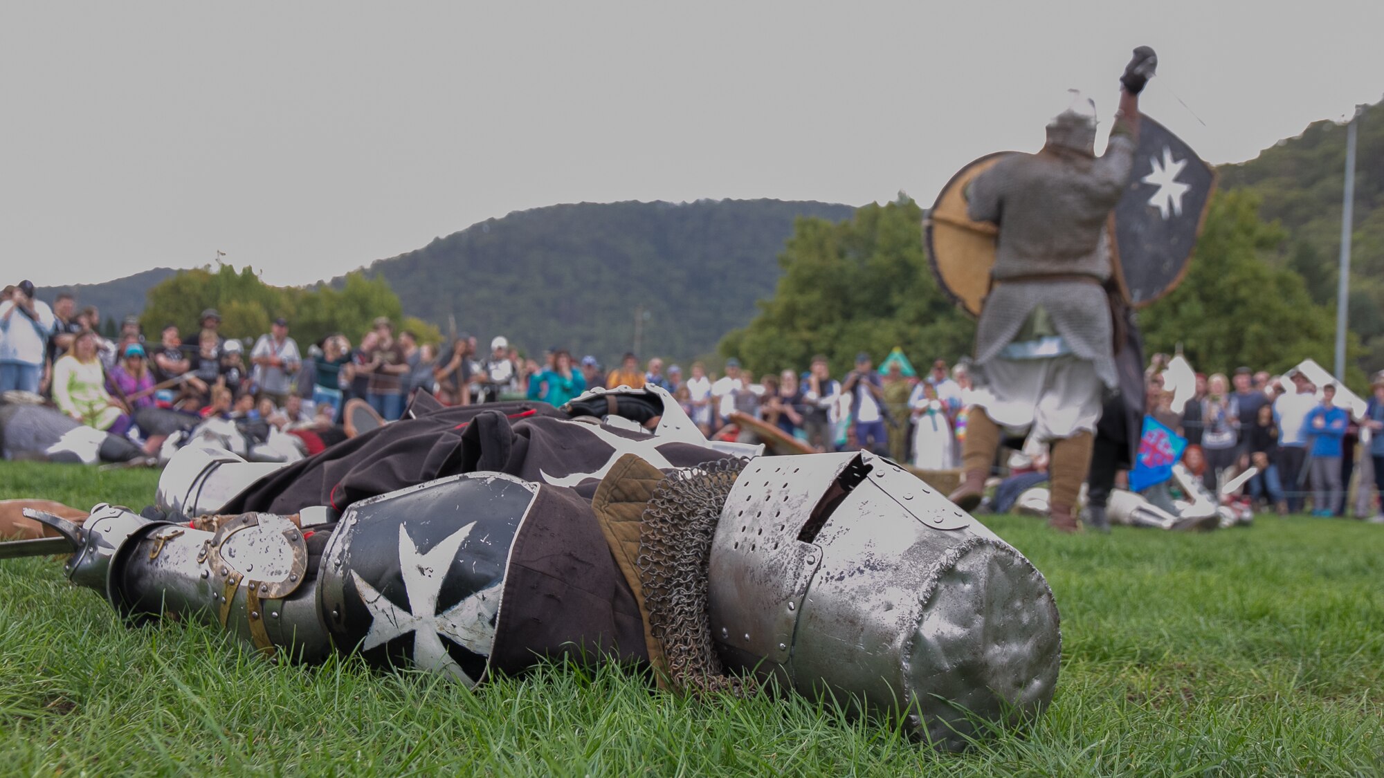 A man in medieval armour and helmet on the ground with another soldier in the background