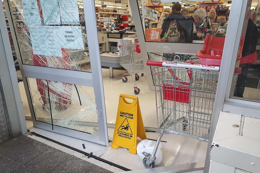 A trolley sits beside a smashed glass door at Coles
