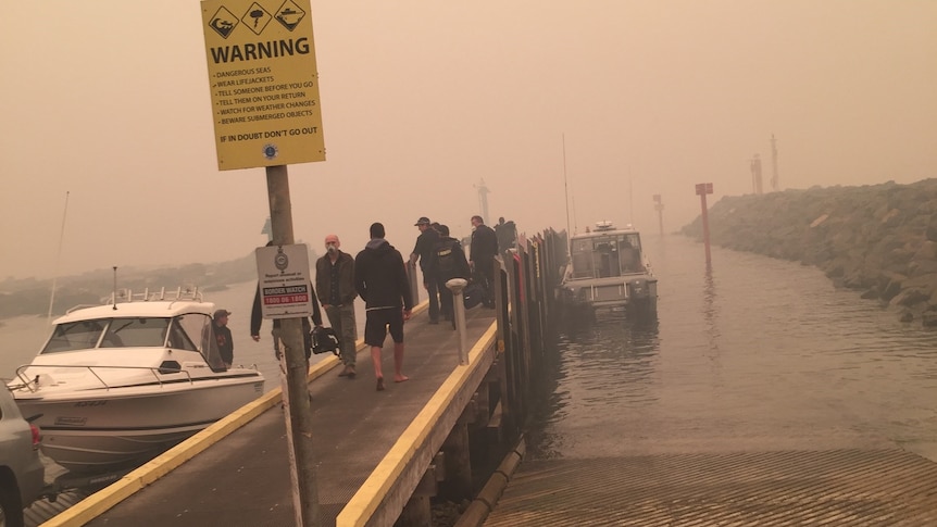 Brown-grey smoke covers a pier, jutting out into the water.