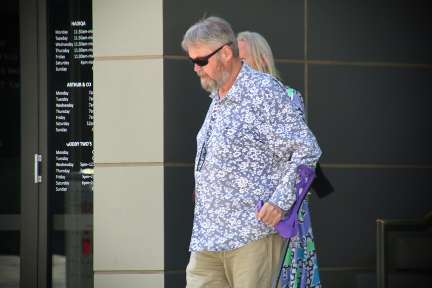 A man in dark glasses and a flower-patterned shirt, walking in front of a courthouse.