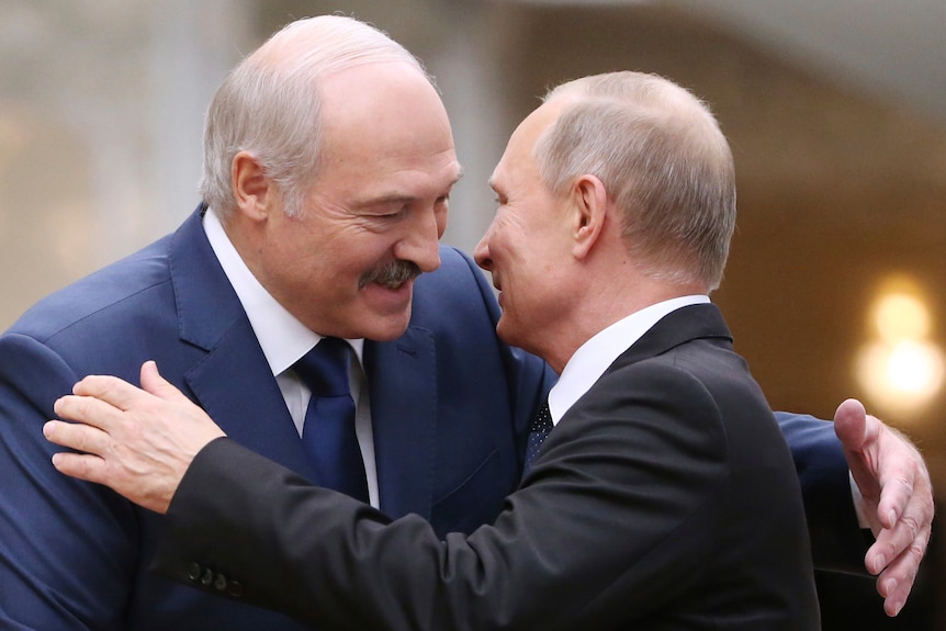 Alexander Lukashenko in blue suit smiles while leaning down to hug Vladimir Putin in black suit