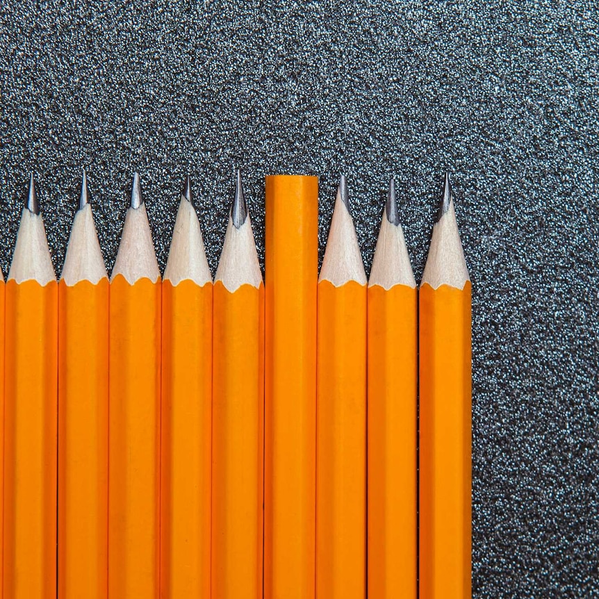 Ten sharp pencils lined up on a grey background.