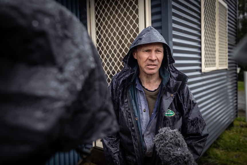 A man in wet weather gear speaks to a member of the media.