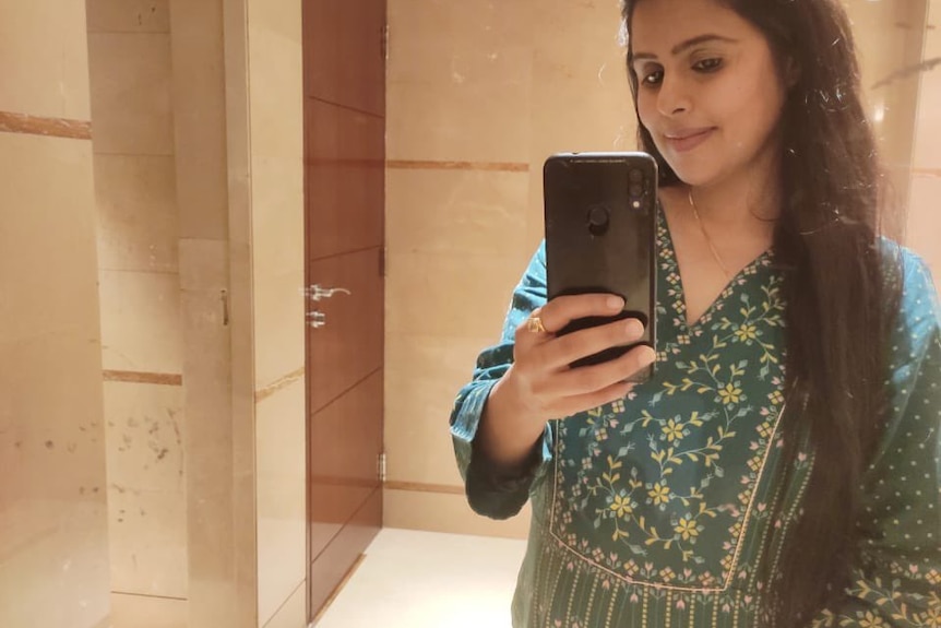 An Indian woman taking a mirror selfie while cradling her pregnant belly 