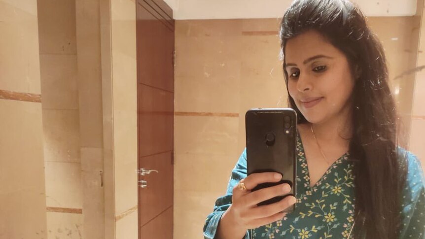 An Indian woman taking a mirror selfie while cradling her pregnant belly 