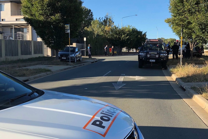 Police car blocks off road with forensic police and vans nearby. Police chat together at crime scene.