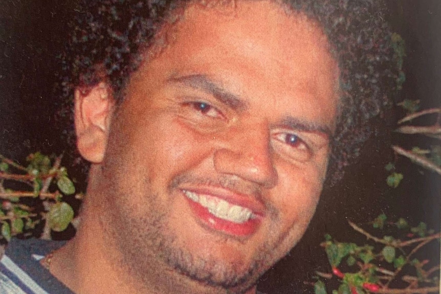 A photo of a smiling Raymond Noel Thomas wearing a silver top outside at night time.