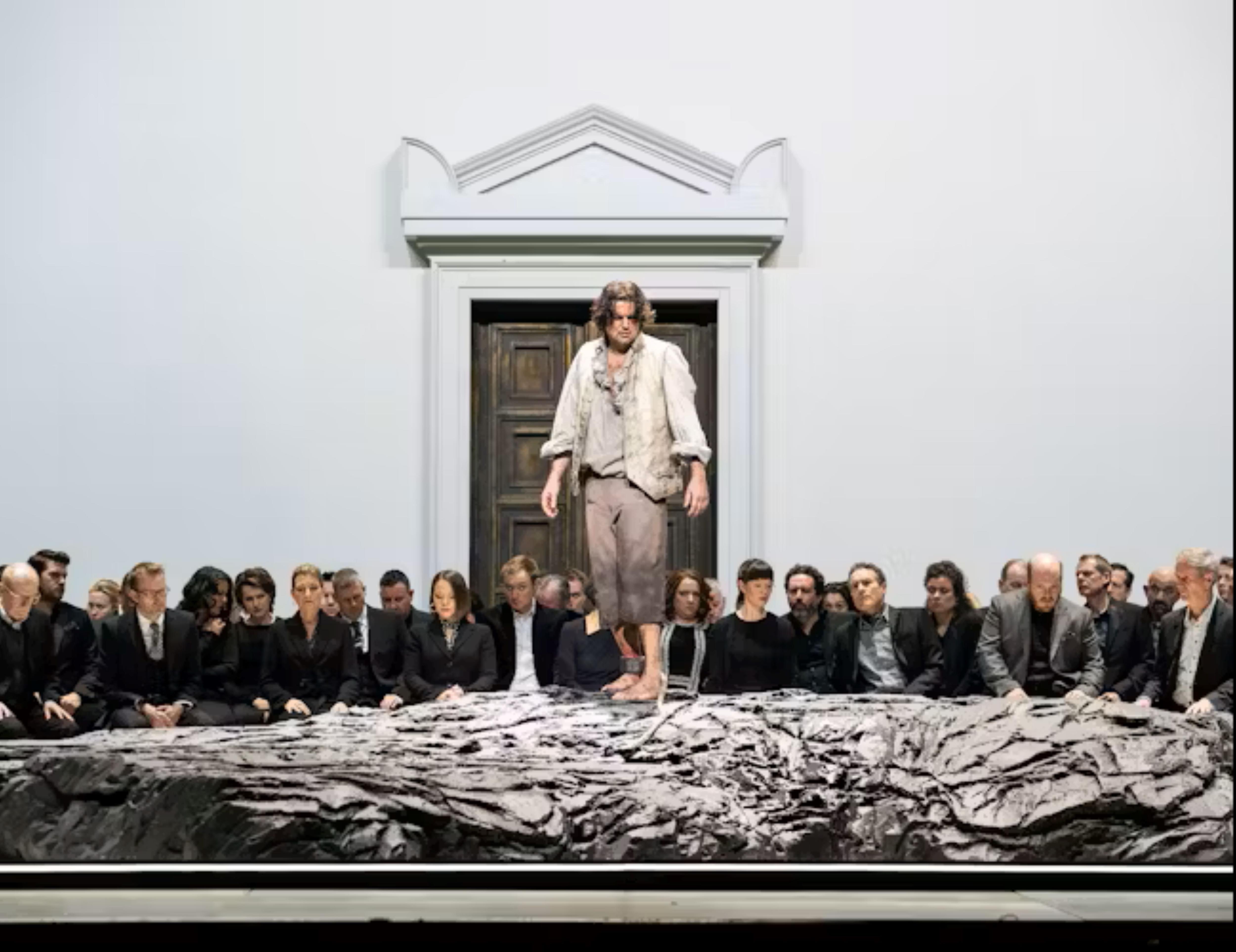 A man stands on a table, from the edge there are twenty or more people looking on.