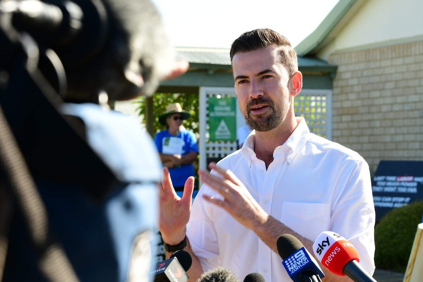 A close up of Zak Kirkup talking to a camera with a volunteer in the background.