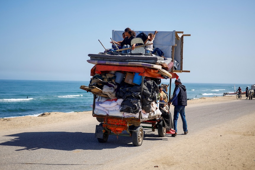 A family pushes a rickshaw stacked with children past a coastline 