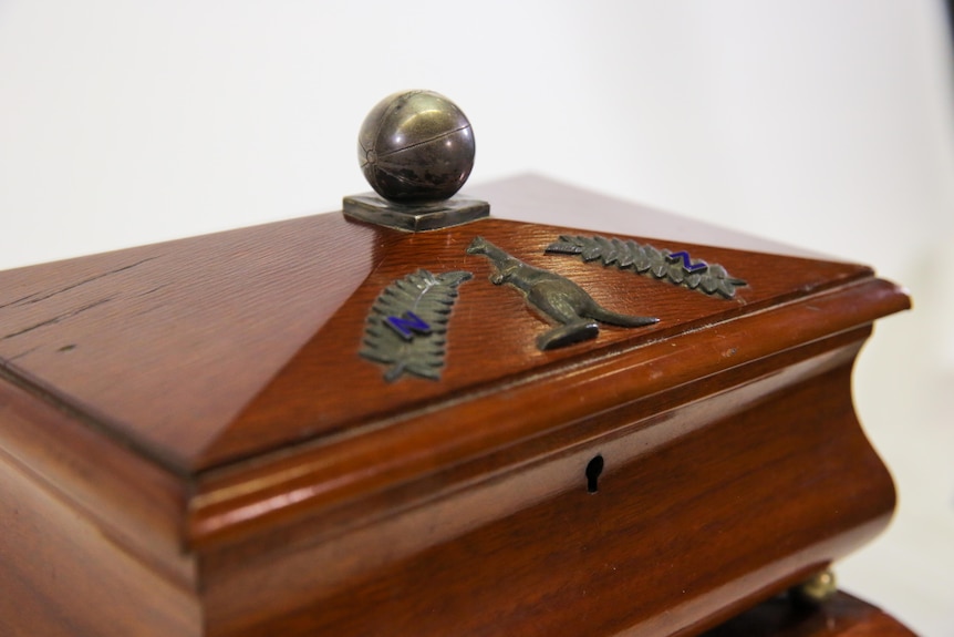 A wooden box lid with a kangaroo and two ferns engraved on the top, with a soccer ball as a handle