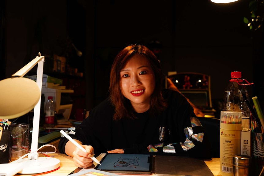 A woman smiles as she looks at the camera, leaning over a desk with an iPad on it.