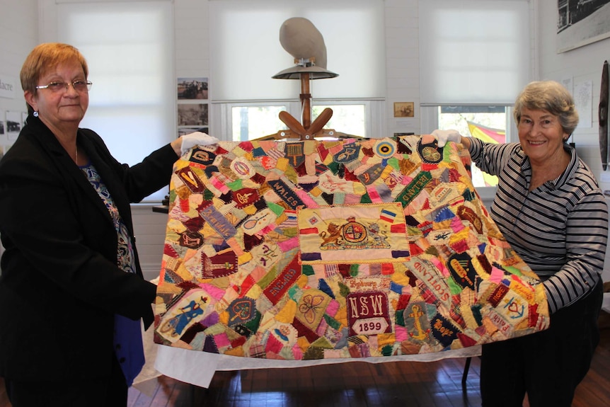 Two women hold colourful quilt