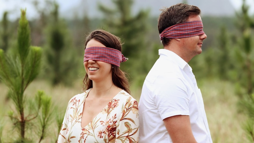 A man and woman stand blindfolded in a paddock