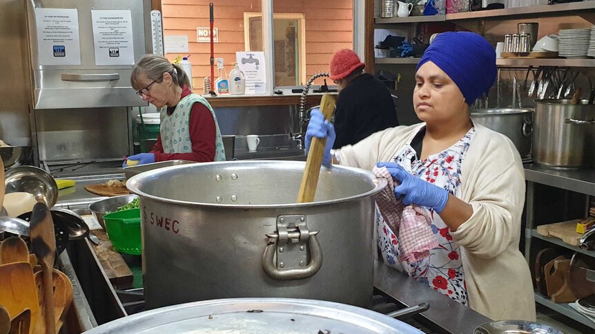 Middle aged Indian woman stirring a large cooking pot in a commercial kitchen