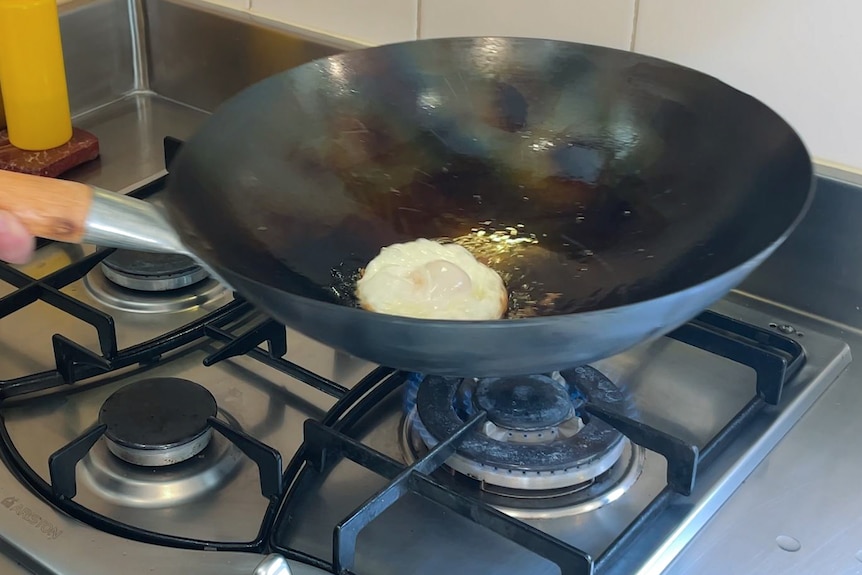 An egg fries in oil at the bottom of a wok, which is on a gas stovetop flame.