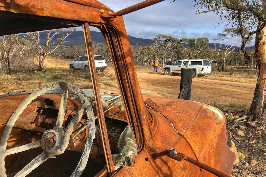 A rusted, burnt-out car on a dirt road.