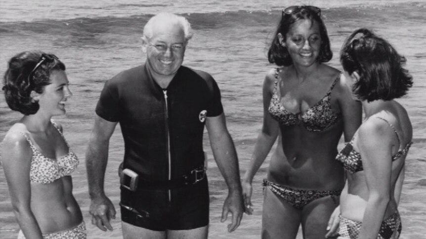 Harold Holt stands with women at the beach