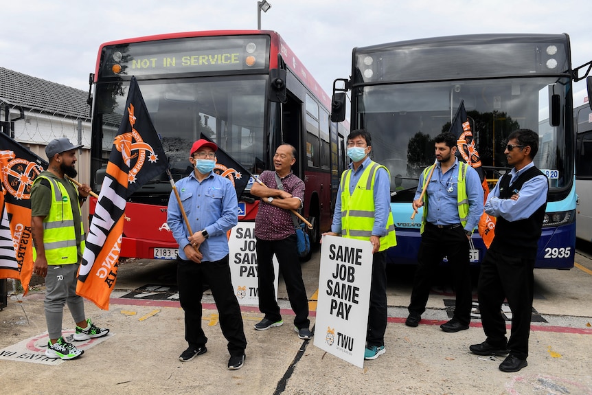 Bus drivers holding banner and flags stand in front of two buses. 