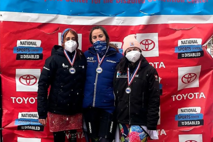 Trois femmes portant des masques, des vestes de ski et des médailles se tiennent côte à côte, regardant la caméra.