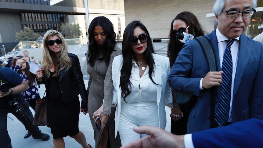 Vanessa Bryant walks out of court wearing a white pantsuit surrounded by lawyers and people with cameras and microphones