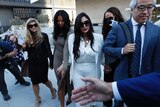 Vanessa Bryant walks out of court wearing a white pantsuit surrounded by lawyers and people with cameras and microphones