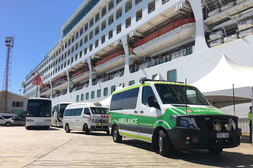 An ambulance is parked on the jetty where a cruise ship is docked.