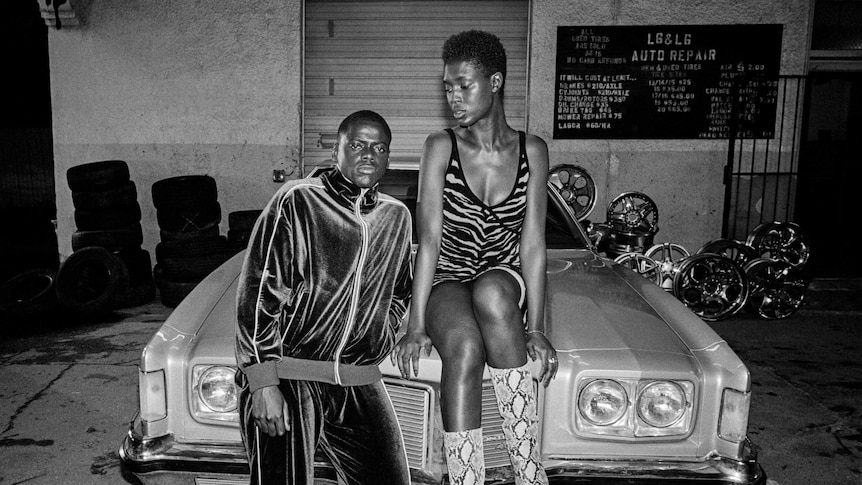 A black and white image from the movie Queen and Slim with Daniel Kaluuya & Jodie Turner-Smith posing on a car
