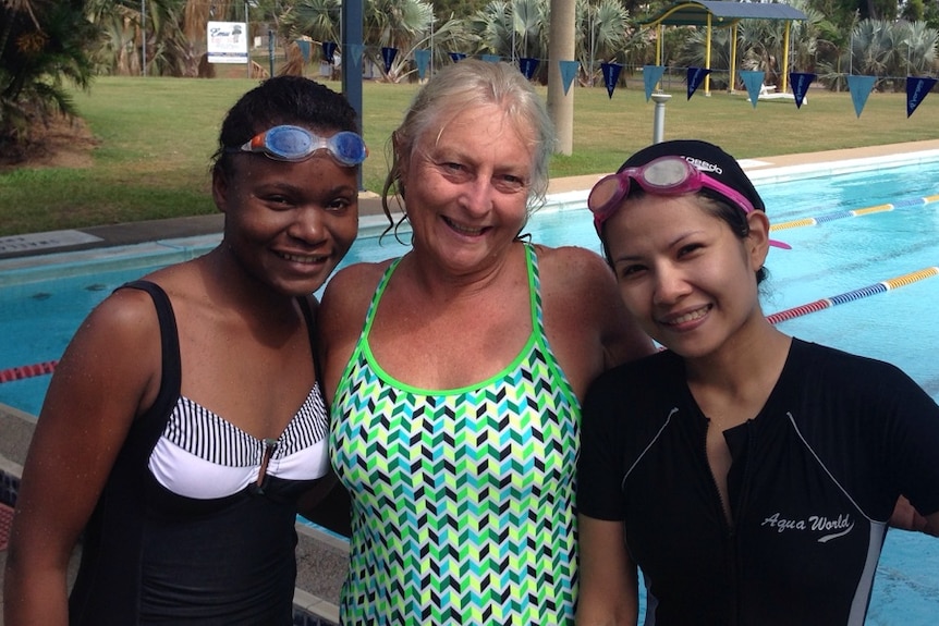 Lynne Barrett wearing a bright swimsuit stands between two women by the swimming pool.