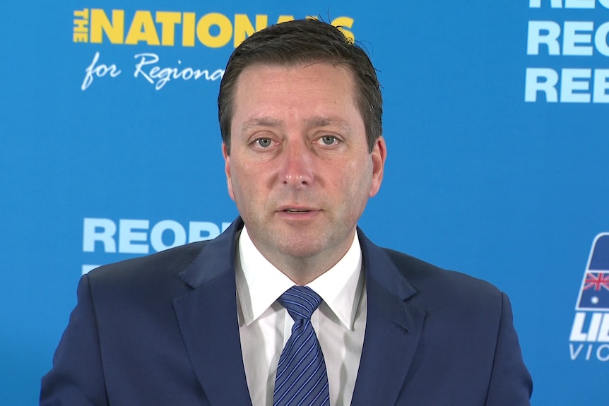 A man in a blue suit in front of a blue backdrop