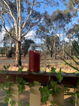 Uma vela vermelha em uma jarra de vidro sobre uma cerca de madeira. 
