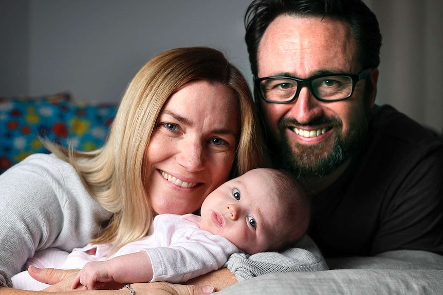 Anna Meares and her partner Nick Flyger smile and cradle their baby daughter Evelyn.