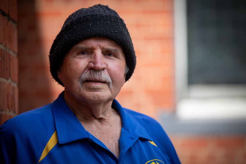 A close-up view of a man wearing a black beanie and blue polo shirt against a red brick wall.